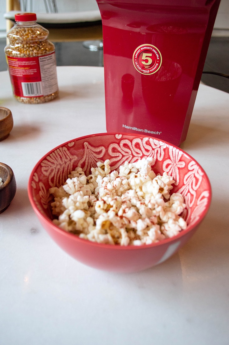 A bowl of popcorn beside a home air-pop popcorn maker.