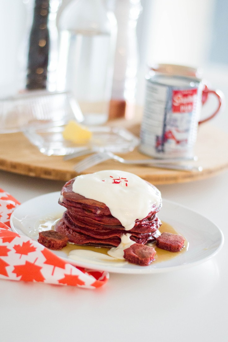A plate with a stack of red velvet pancakes with a maple syrup buttercream topping.