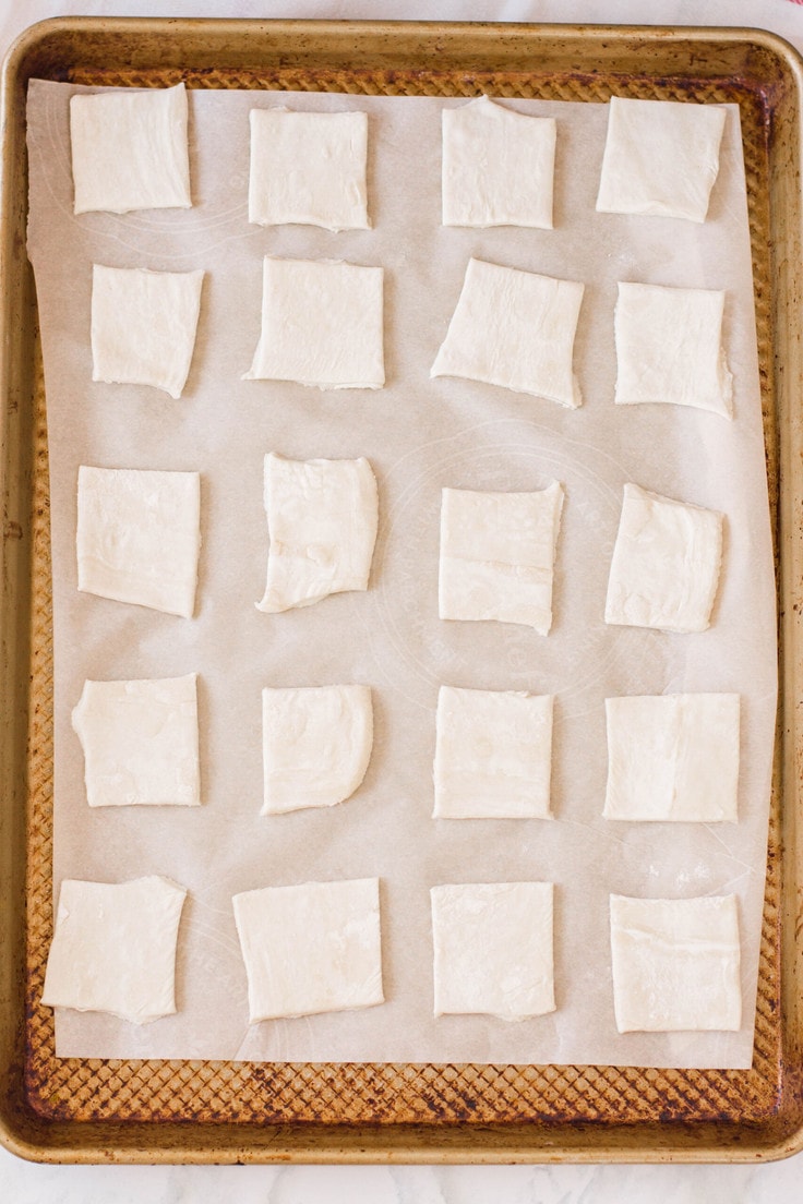 Uncooked puff pastry squares on a baking sheet.