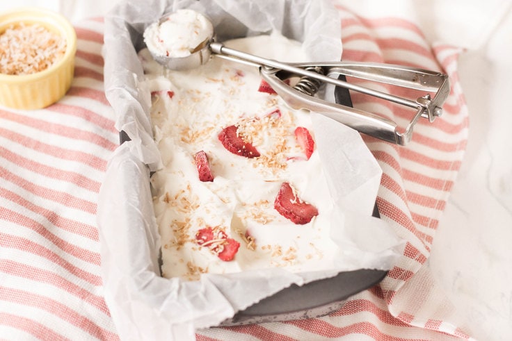 A metal pan full of ice cream with pieces of strawberry on top.