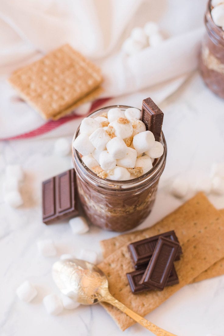 A glass mason jar full of pudding and topped with marshmallows, graham cracker crumbs, and Hershey bar pieces.