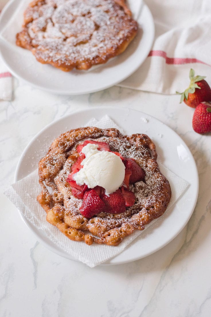 Funnel cake on a plate with strawberries and vanilla ice cream.