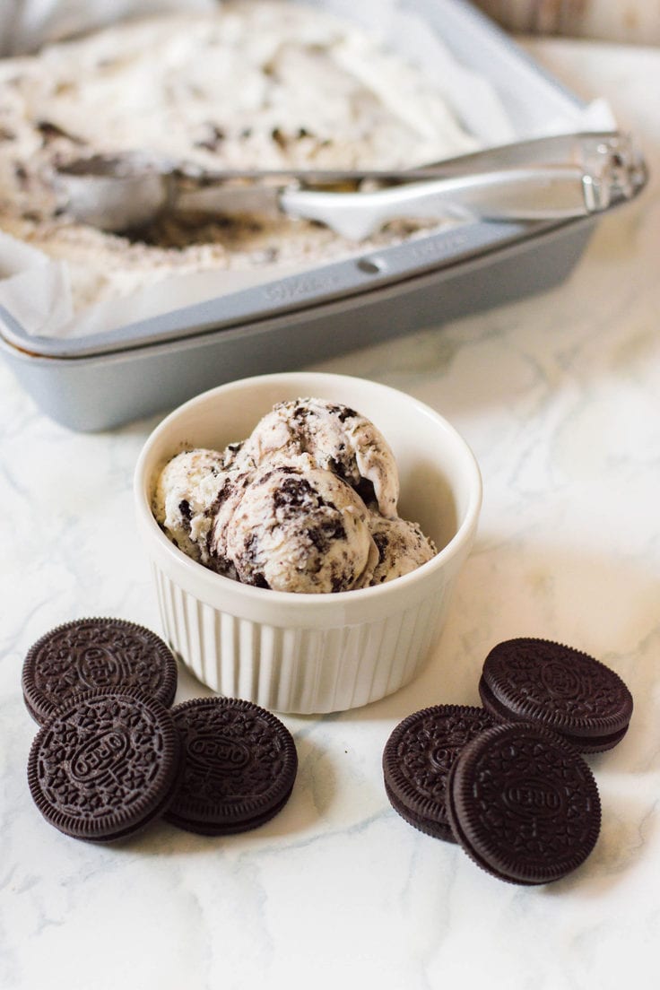 Oreo cookie ice cream in a bowl beside a cake pan full of frozen ice cream.
