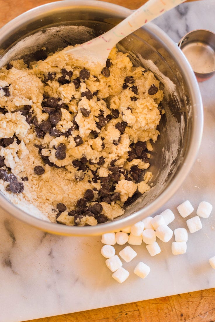 Chocolate chip cookie dough in a bowl beside mini marshmallows.