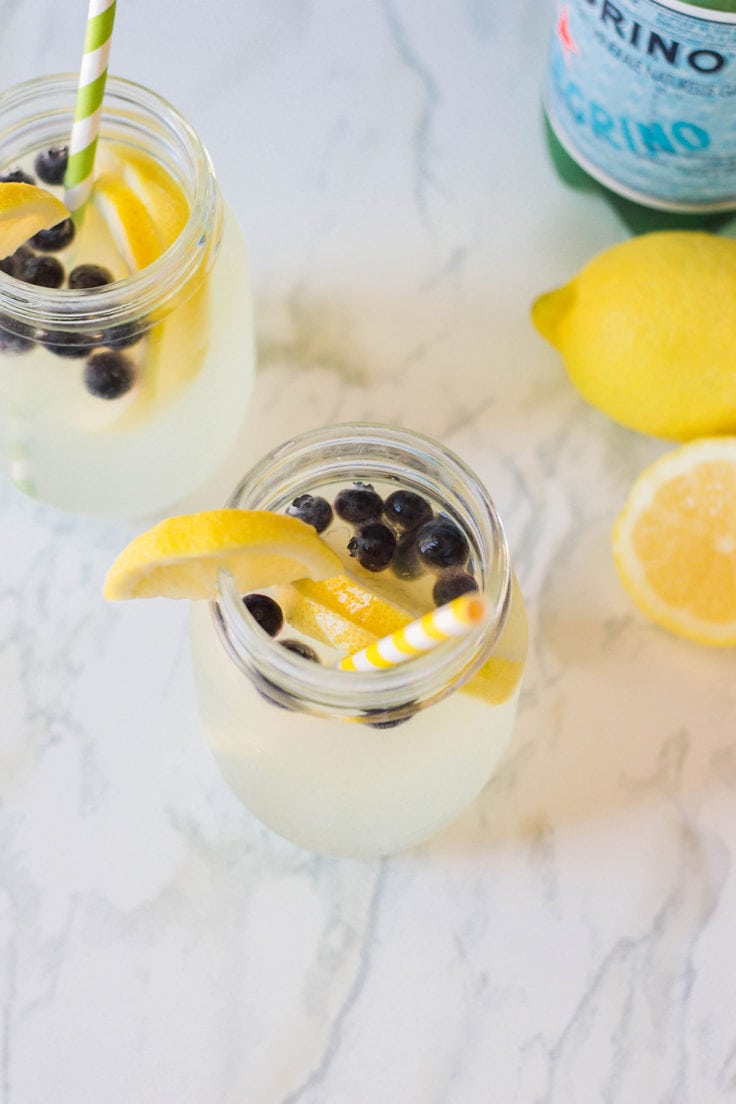 A glass of blueberry lemonade with a lemon wedge on the rim.