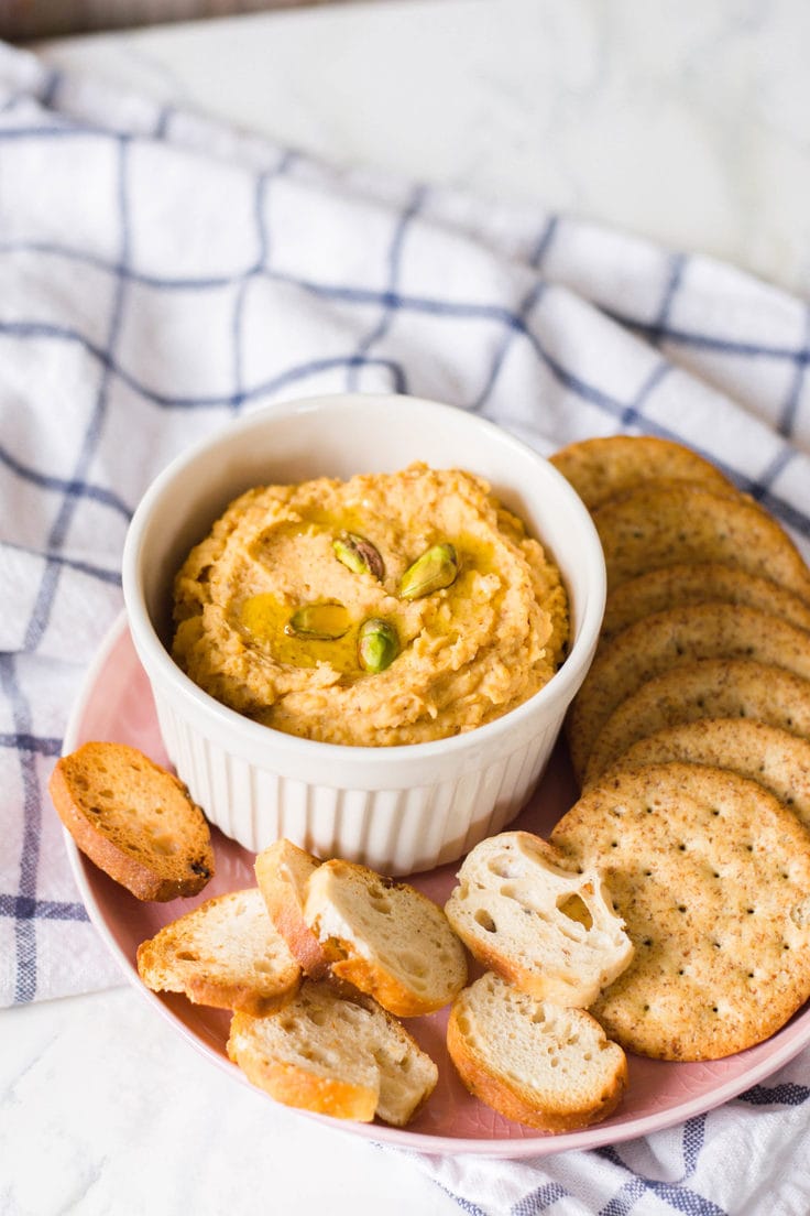 A bowl of sweet potato hummus with crackers and bread.