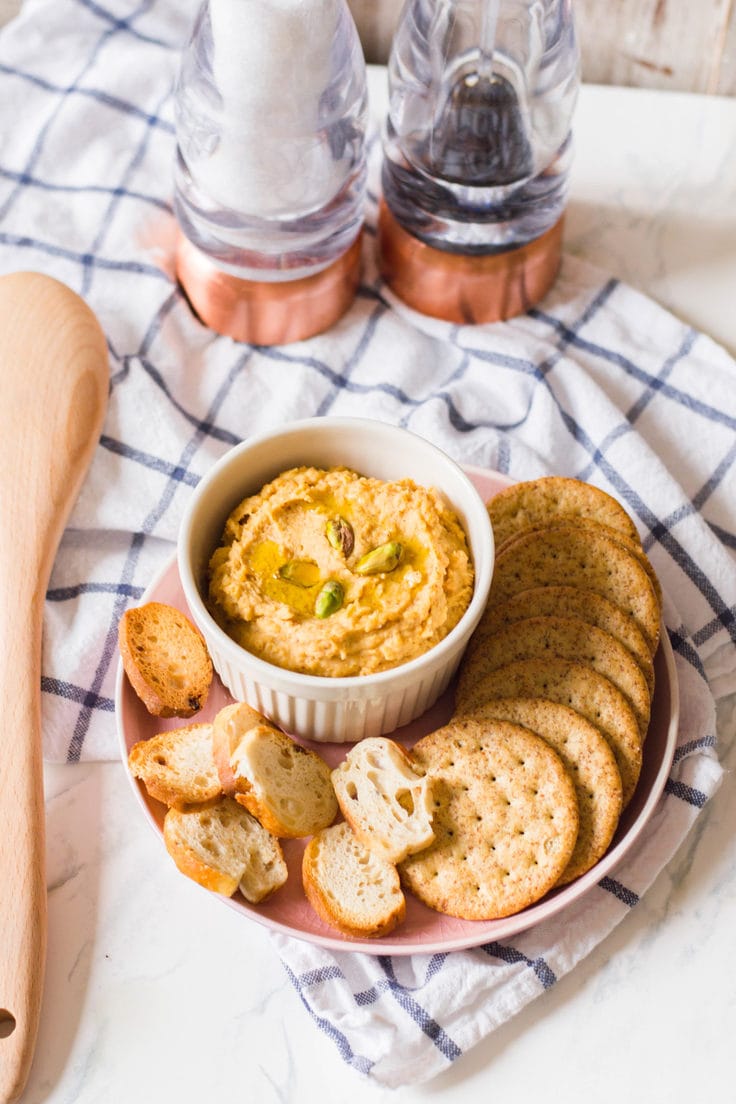 A bowl of sweet potato hummus with crackers and bread.