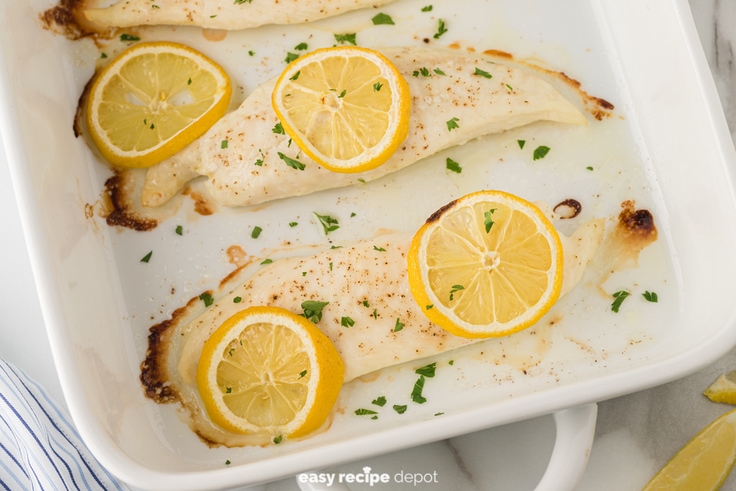 oven baked tilapia with lemon slices in a casserole dish