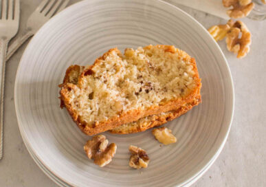 Bird's eye view of slices of walnut loaf, on a grey plate with a few walnuts around it.