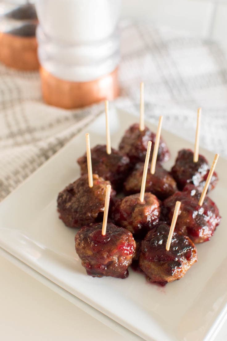 Meatballs with a toothpick in each one, sitting on a white square plate