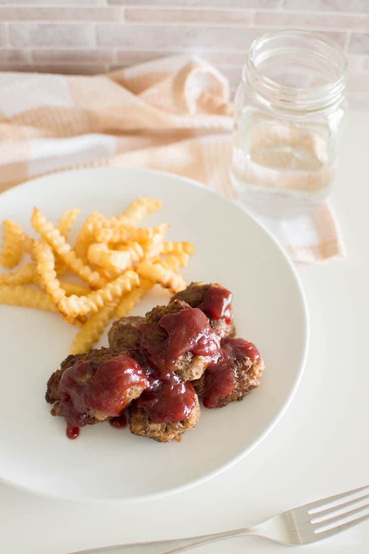 Bird's eye view of homemade beef meatballs, with a cranberry sauce topping on a white plate with a side of fries