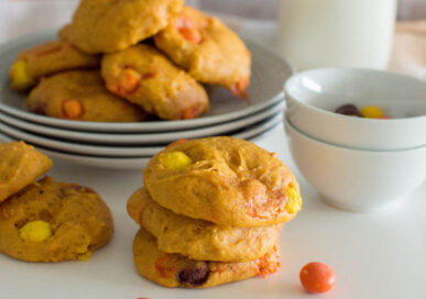 A stack of easy pumpkin cookies surrounded by a plate full of more cookies and a bowl of candy