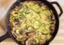 Aeriel view of a vegetable frittata in a black cast iron skillet, sitting on top of a wooden cutting board