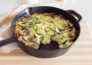 A cast iron skillet frittata, filled with mushrooms and zucchini, with a piece cut out of it