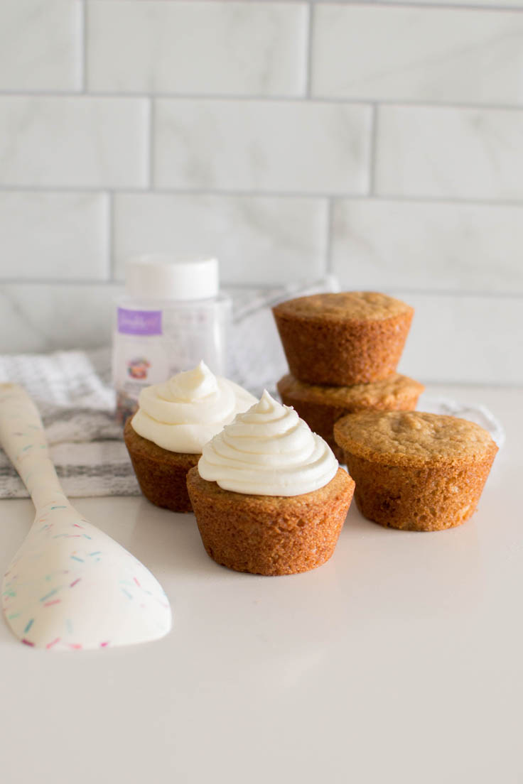 Vanilla frosting topping on two vanilla cupcakes with plain cupcakes in the background
