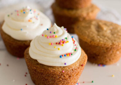 Vanilla icing swirled on top of a vanilla cupcake and topped with sprinkles, surrounded by additional cupcakes