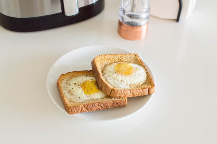 Two slices of air fryer egg toast on a small white plate with an air fryer and a pepper grinder in the background