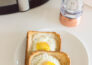 Ariel view of two slices of egg toast on a white plate with an air fryer and pepper grinder in the background