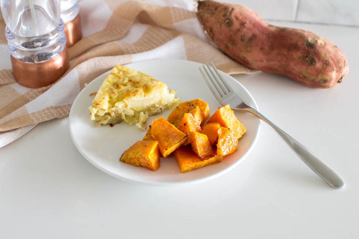 Maple roasted sweet potatoes being served as a side dish on a white plate with a frittata