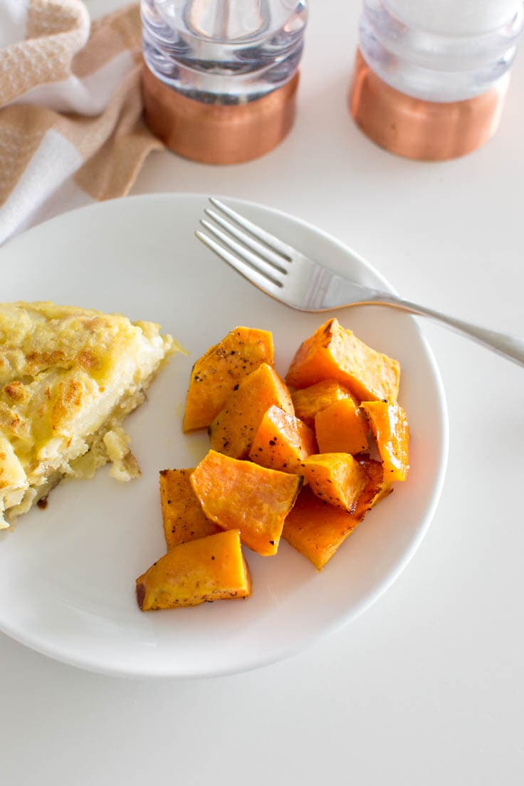 Bird's eye view of maple roasted sweet potatoes on a white plate, next to a piece of frittata and a fork