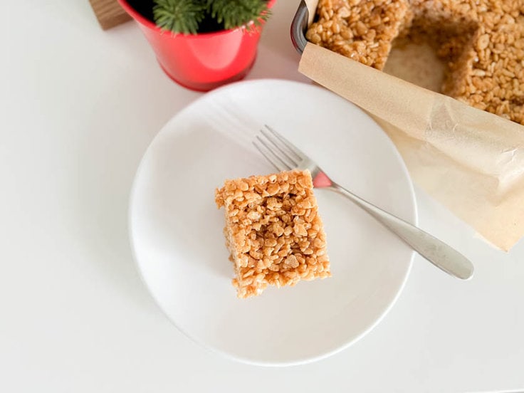 A gingerbread-flavored rice cereal treat on a white plate with a fork sitting next to it