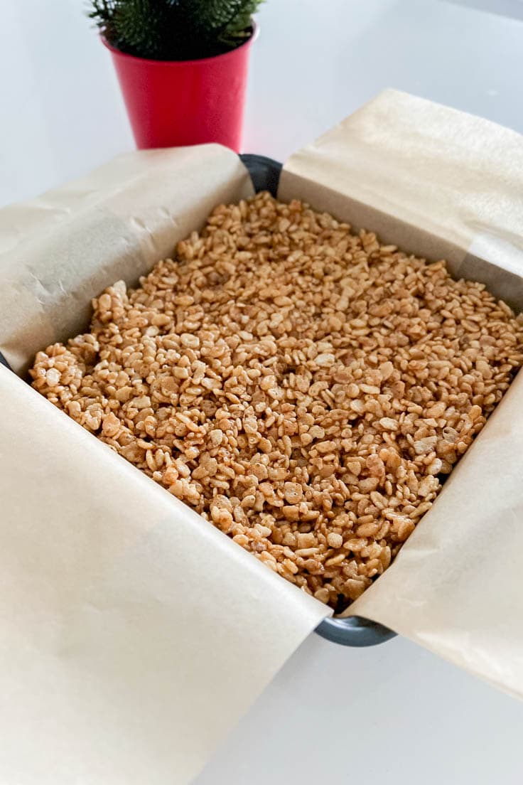 Gingerbread Rice Krispie Treats smoothed out in a parchment-lined square pan
