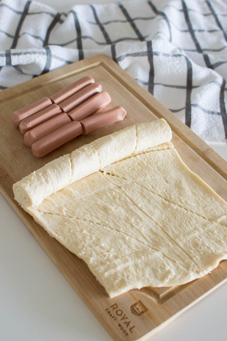 Canned croissant dough and hot dogs on a wooden cutting board