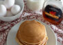 Aerial view of stacked pancakes with syrup, milk and eggs surrounding it