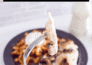 A fork holds a piece of oven-baked chicken, with the full meal sits in the background on a grey plate