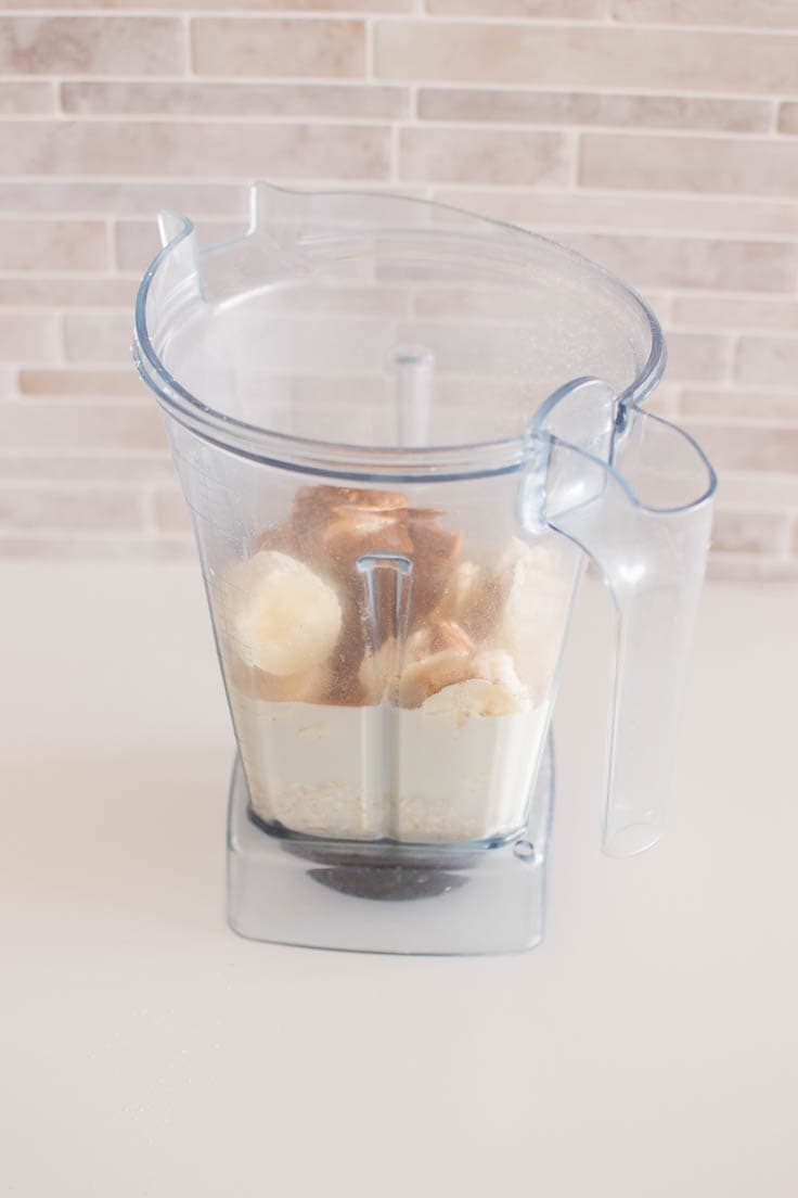 Adding bananas, oat milk, peanut butter and ground cinnamon to a blender