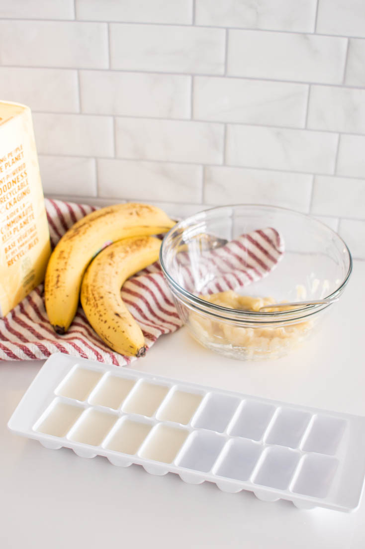 Almond milk poured into an ice tray, accompanied by a glass bowl of mashed bananas