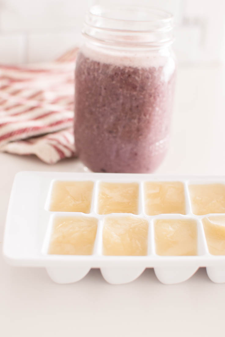 Almond milk frozen in an ice cube tray, with a berry smoothie in the background