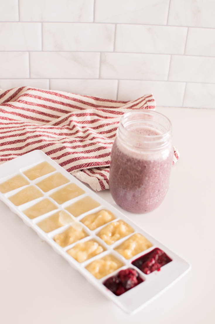 Almond milk, mashed bananas, and mashed berries frozen in a white ice cube tray, accompanied by a smoothie