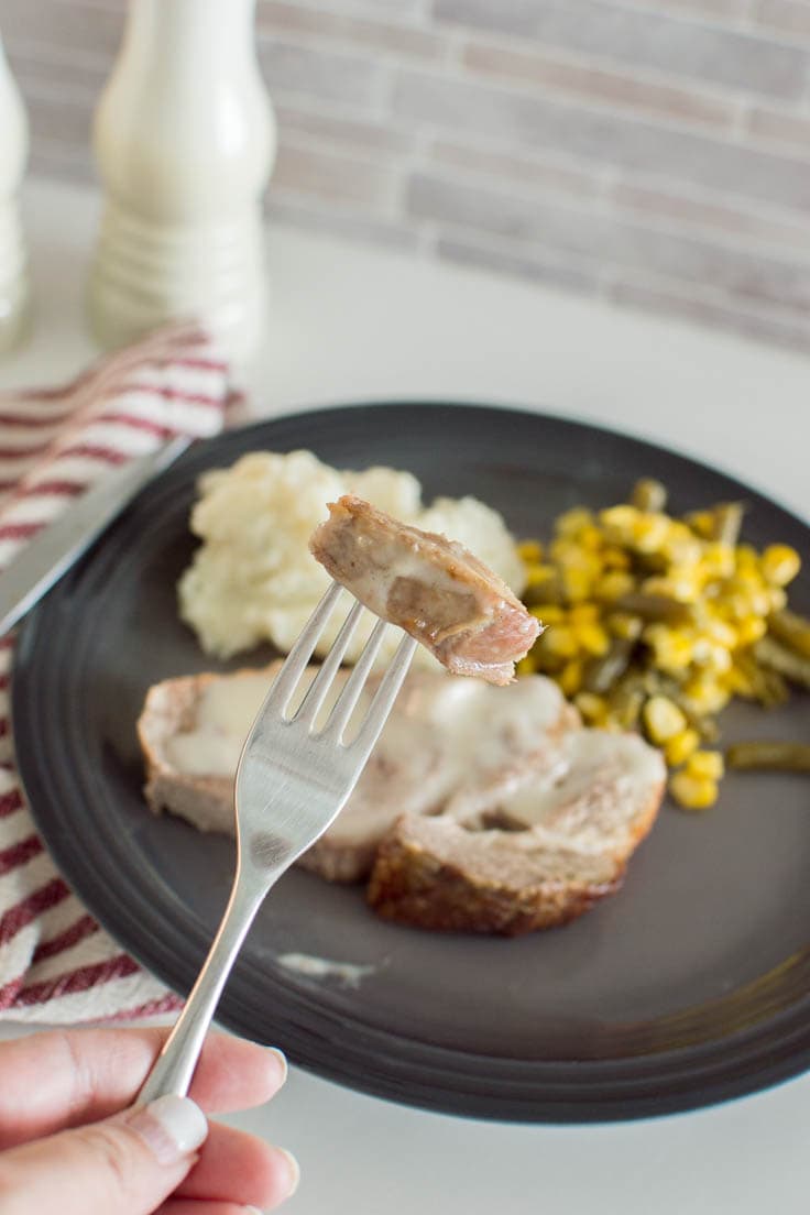 A piece of baked pork on a fork, with the entire meal on a grey plate sitting in the background