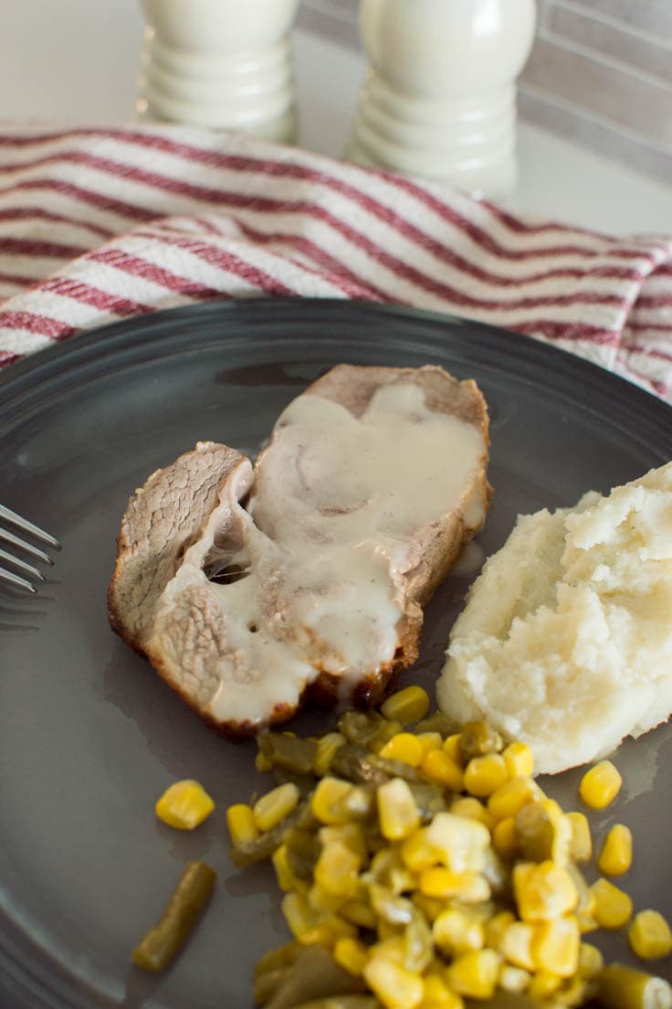 A pork chop slice covered with homemade gravy on a grey plate