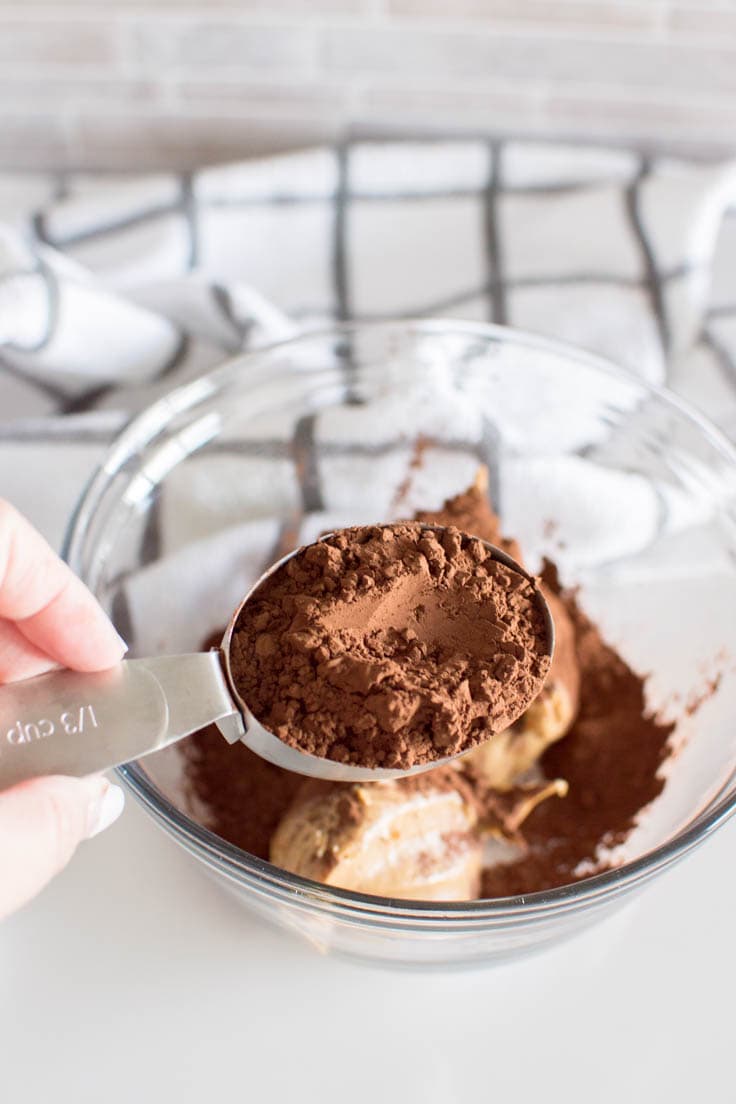 Using a measuring cup to scoop cocoa powder to make a batch of no-bake brownie bites