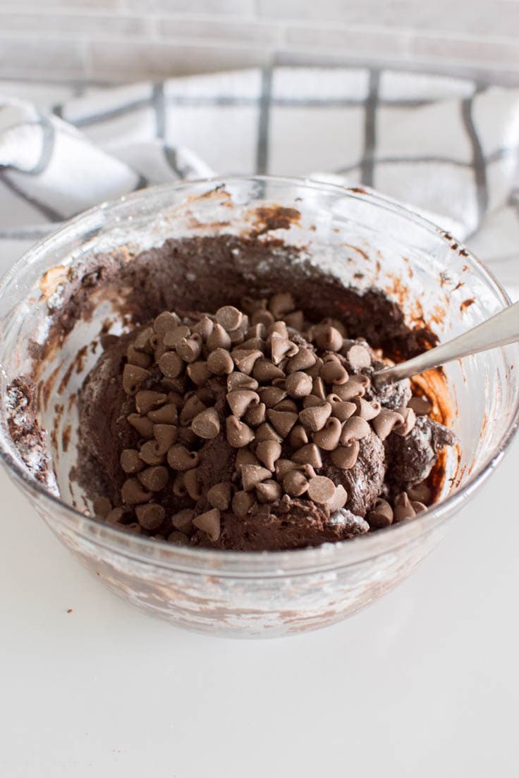 Adding chocolate chips to a bowl of brownie bites batter
