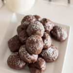 Aerial view of a pile of no-bake brownie bites on a white square plate with a glass of milk in the background