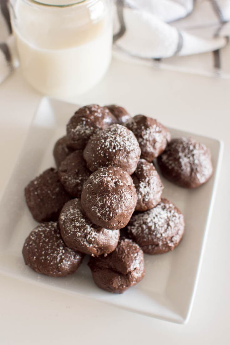 Aerial view of a pile of no-bake brownie bites on a white square plate with a glass of milk in the background