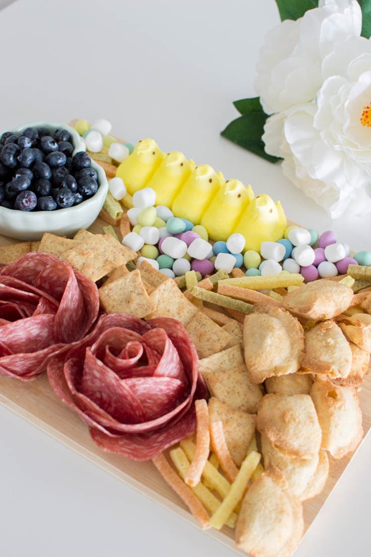 A spring charcuterie board, which includes Peeps, candy eggs, fruits, and salami roses