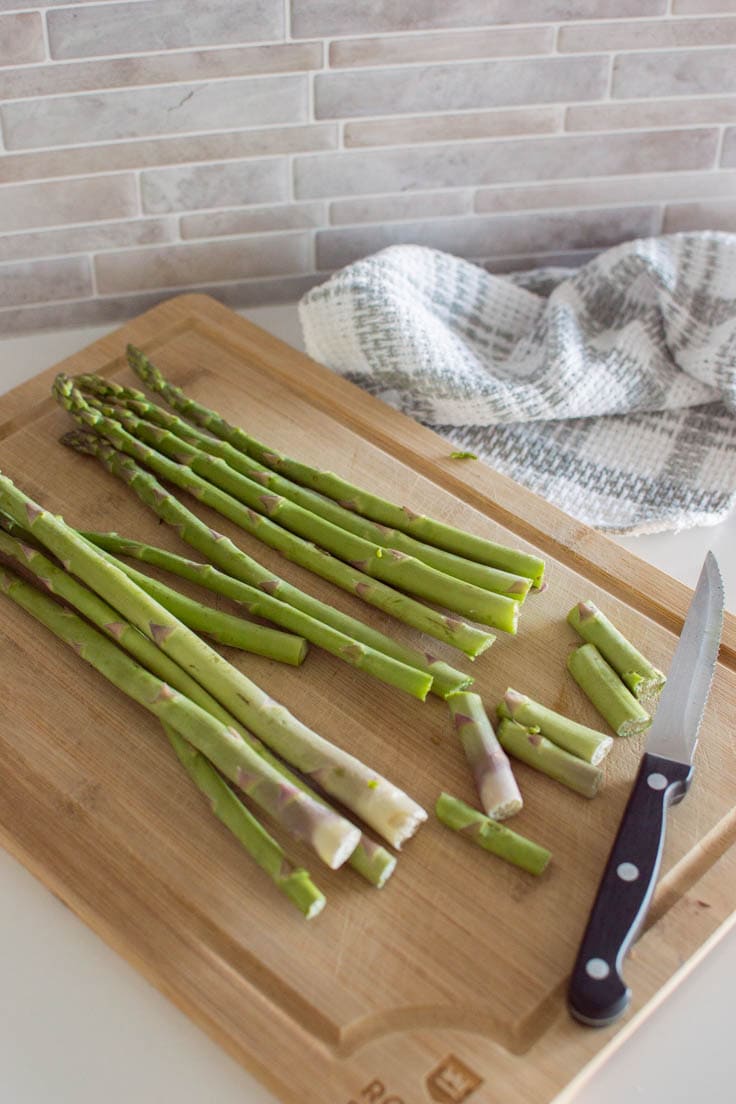 Cutting off asparagus ends on a wooden cutting board.