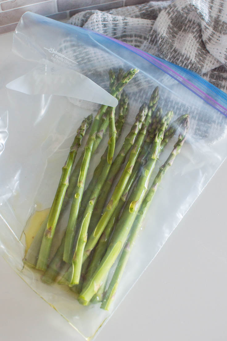 Adding asparagus and olive oil into a freezer bag to evenly coat the asparagus