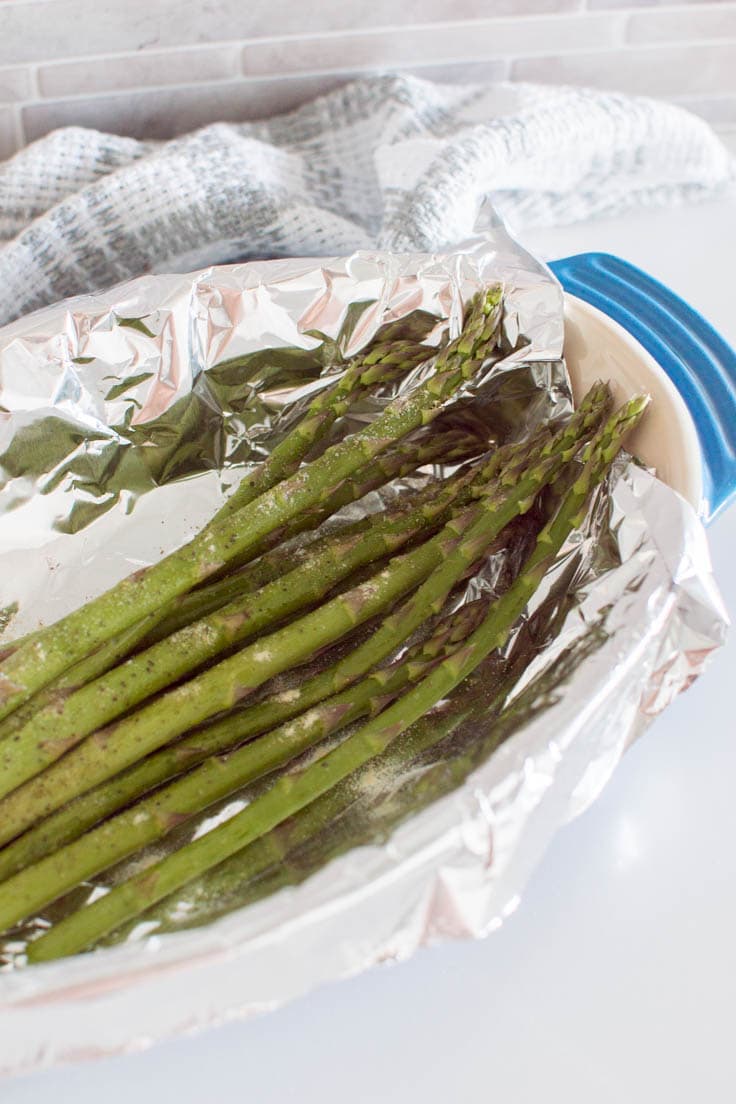 A bunch of asparagus sitting in a tin foil-lined pan, ready to be roasted in the oven