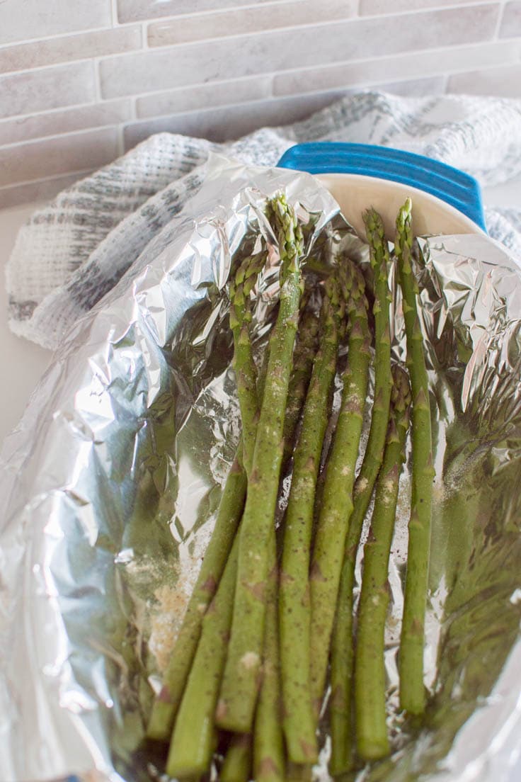 A bunch of asparagus sitting in a tin foil-lined pan, ready to be roasted in the oven
