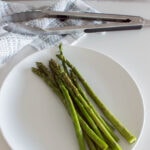 Aerial shot of oven-roasted asparagus ready to be served on a white plate with tons in the background