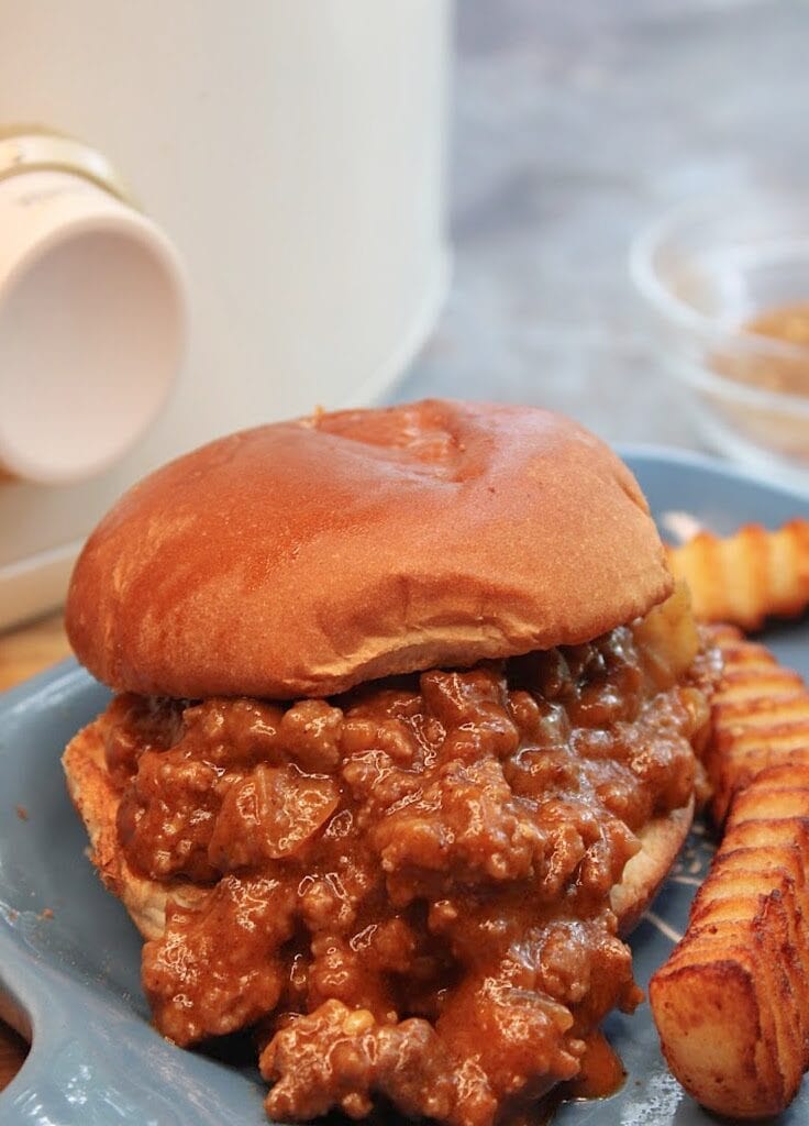 A sloppy joe on a blue plate with french fries 