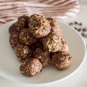 A stack of Date Energy Balls on a white plate, with a striped tea towel and chocolate chips in the background