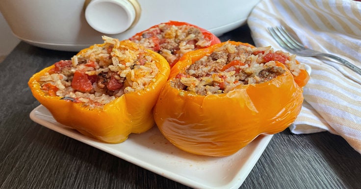 yellow and orange stuffed peppers on a white plate with yellow and white striped napkin