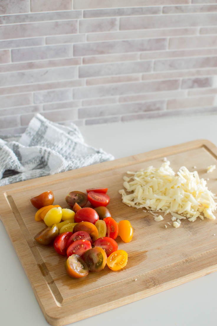 Cherry tomatoes and shredded cheese on a wooden cutting board
