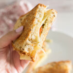 A hand holding a serving of Pesto Grilled Cheese Sandwich